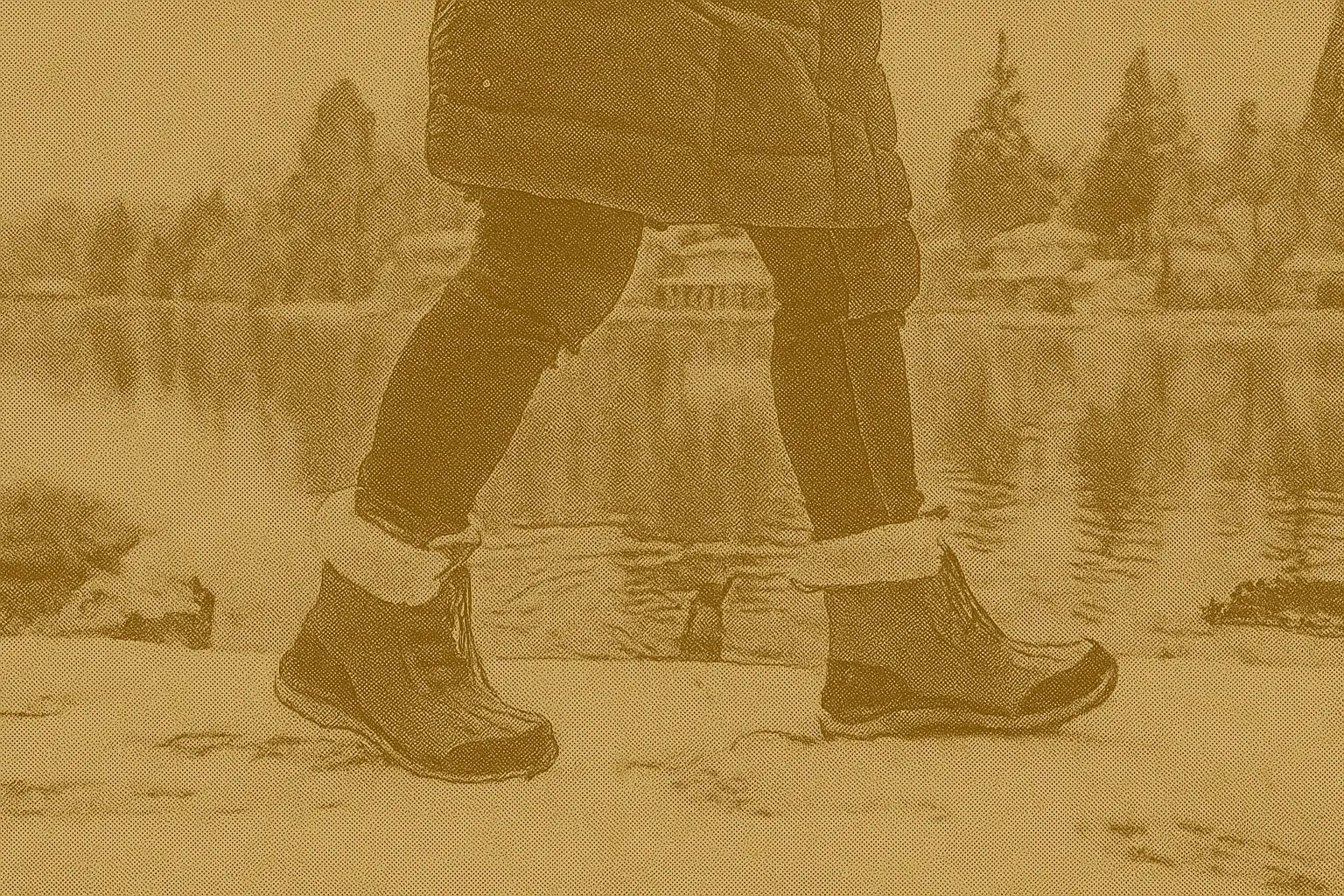 Person wearing brown winter boots walking on snowy ground near a frozen lake in Canada, demonstrating traction and warmth.
